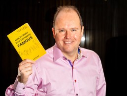 Jon Card holding his book How To Make Your Company Famous